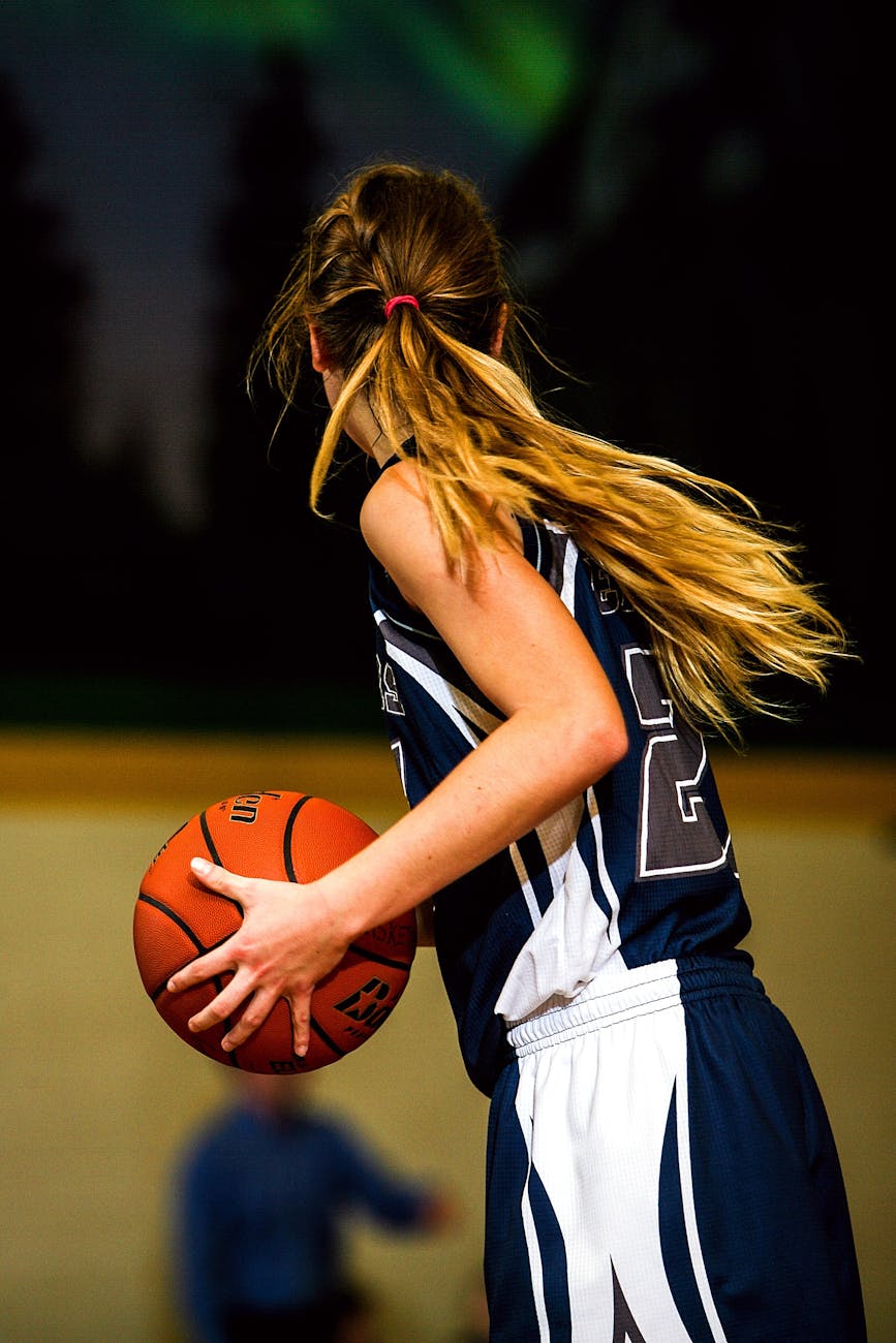 woman in blue and white basketball jersey holding brown basketball